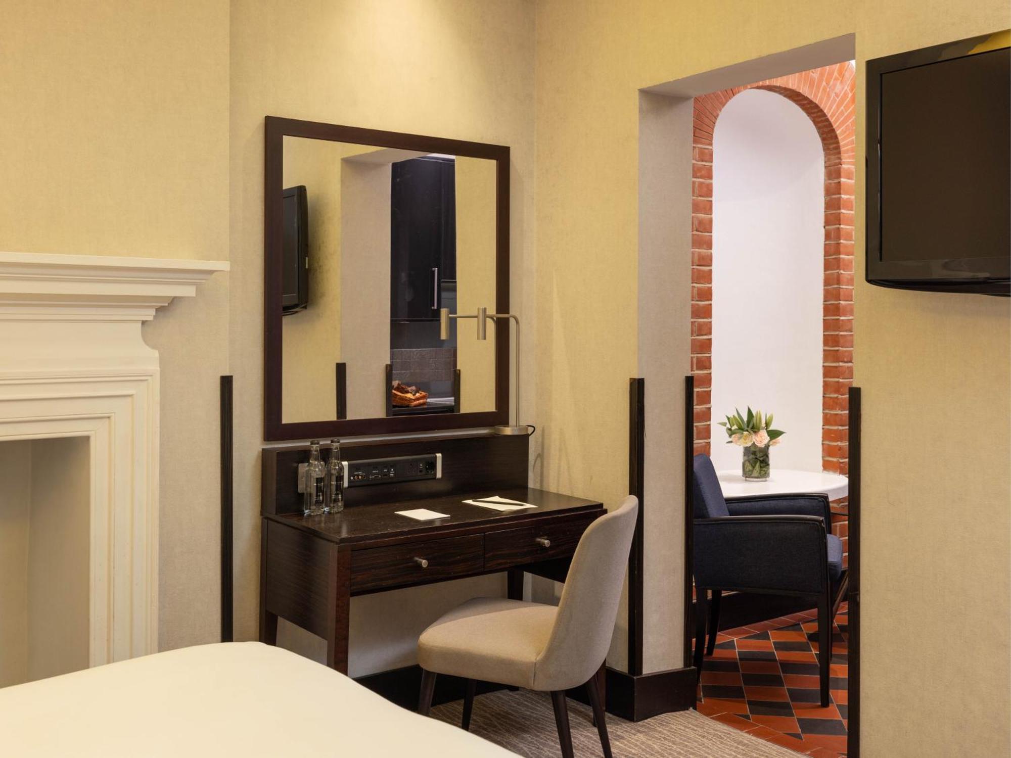 Hotel Montcalm Brewery Townhouse Londýn Exteriér fotografie The photo displays a hotel room setup. On the left side, there's a bed with a simple white bedding arrangement. Adjacent to the bed, there's a wooden desk with a chair, along with a mirror above the desk. The desk area is equipped with some glassware