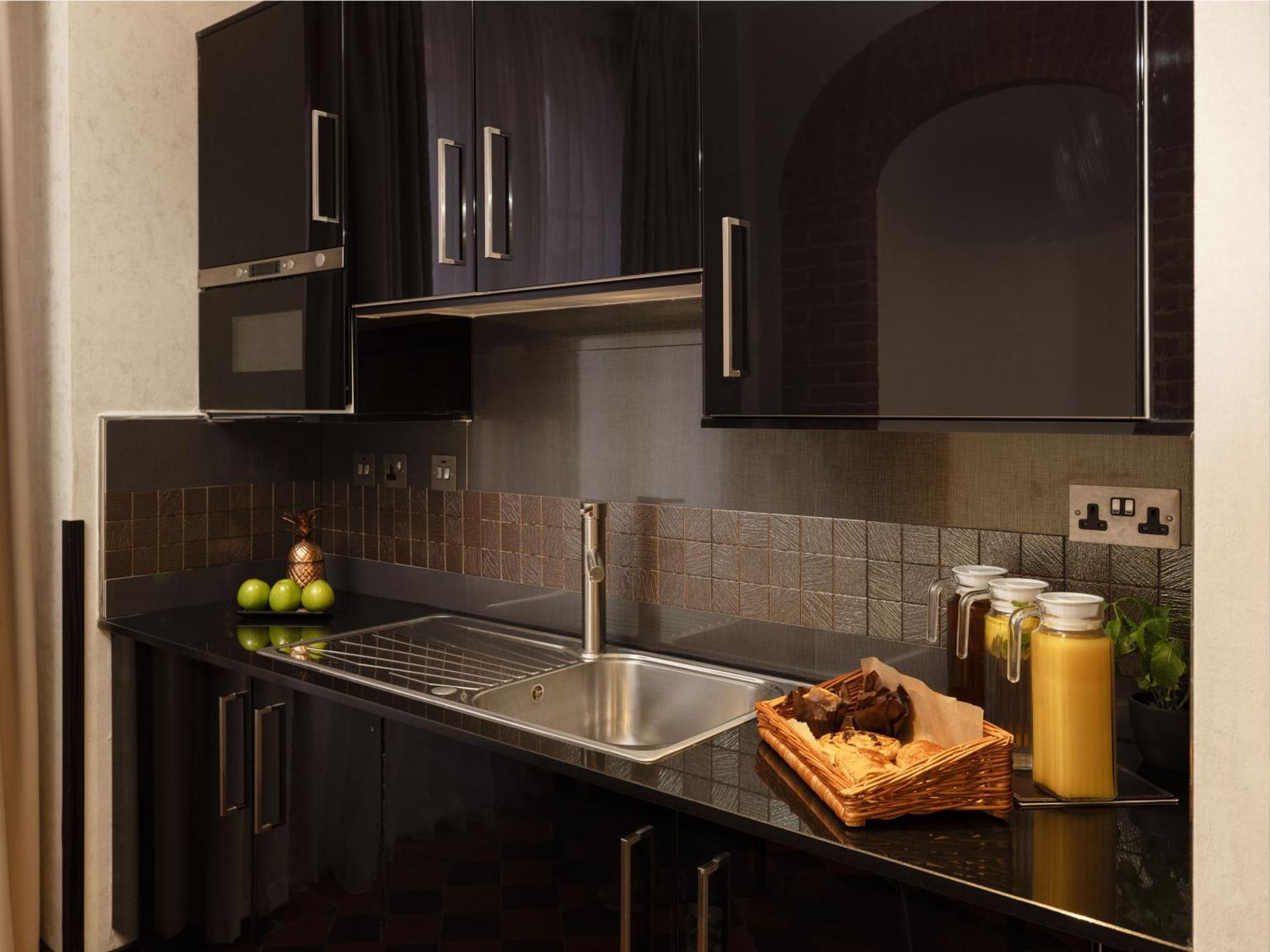 Hotel Montcalm Brewery Townhouse Londýn Exteriér fotografie The photo shows a modern kitchen with sleek black cabinetry and a glossy finish. The kitchen features a stainless steel sink with a contemporary faucet, set against a dark, textured countertop. Above the counter, there are cabinets that match the cou