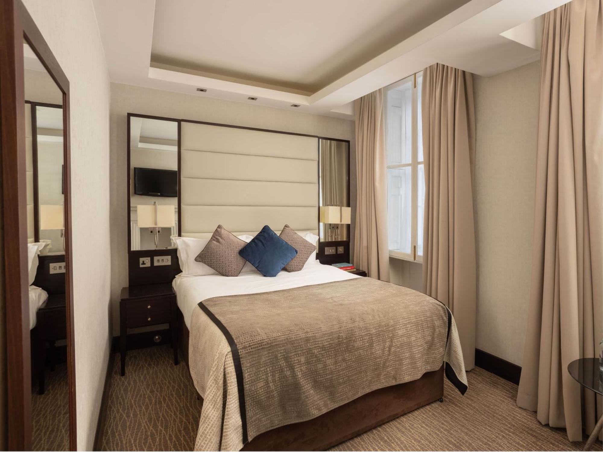 Hotel Montcalm Brewery Townhouse Londýn Exteriér fotografie The photo shows a cozy hotel room with a bed as the focal point. The bed is made with neutral-colored linens and has several pillows, including a decorative blue one. There are bedside tables on either side of the bed, each with a lamp. A large mirro