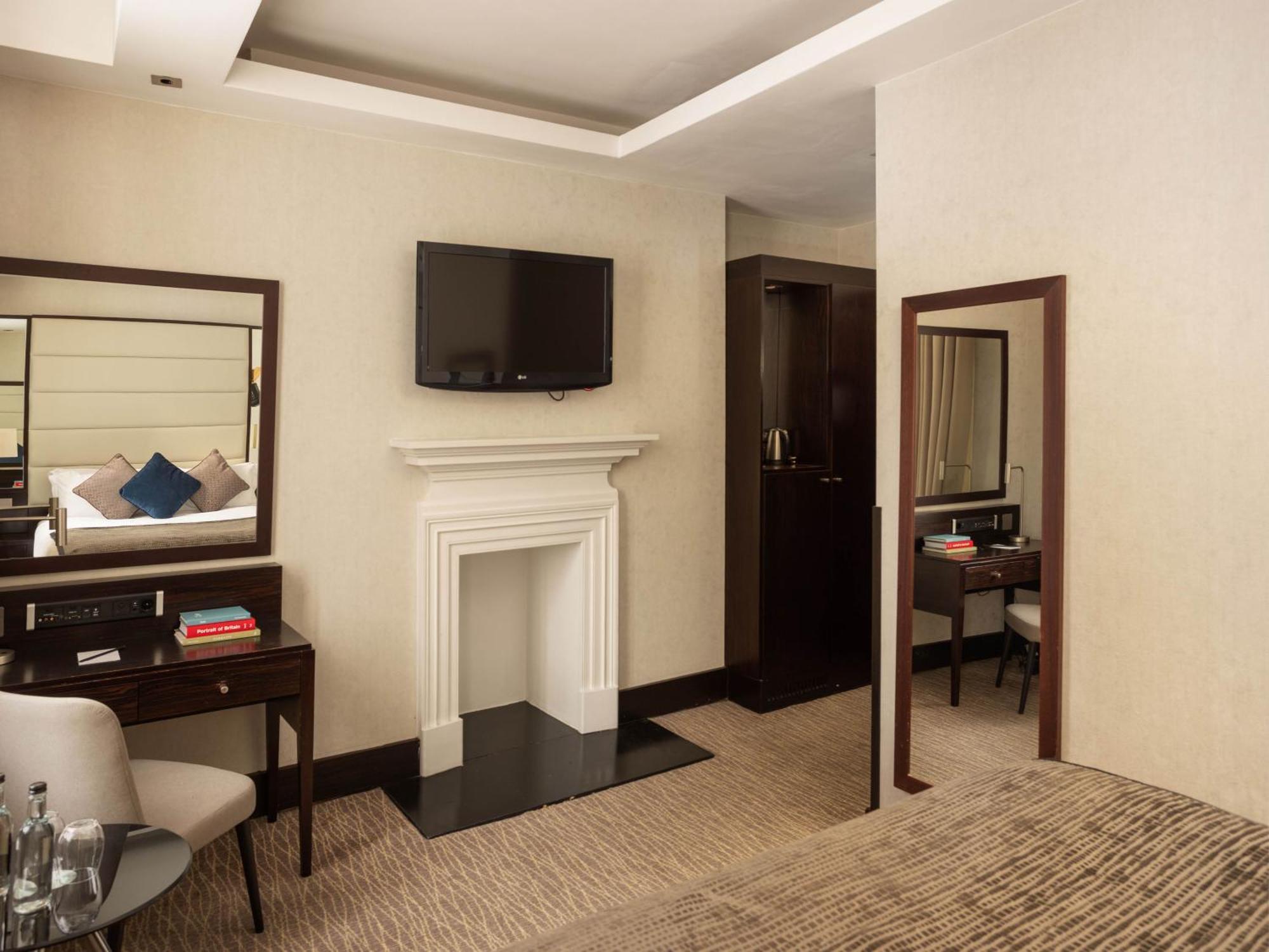 Hotel Montcalm Brewery Townhouse Londýn Exteriér fotografie The photo depicts a stylish hotel room. It features a double bed, a large flat-screen TV mounted on the wall, and a decorative fireplace. There is a wooden desk with a chair beside it, as well as a mirror hanging on the wall. The decor is modern and 